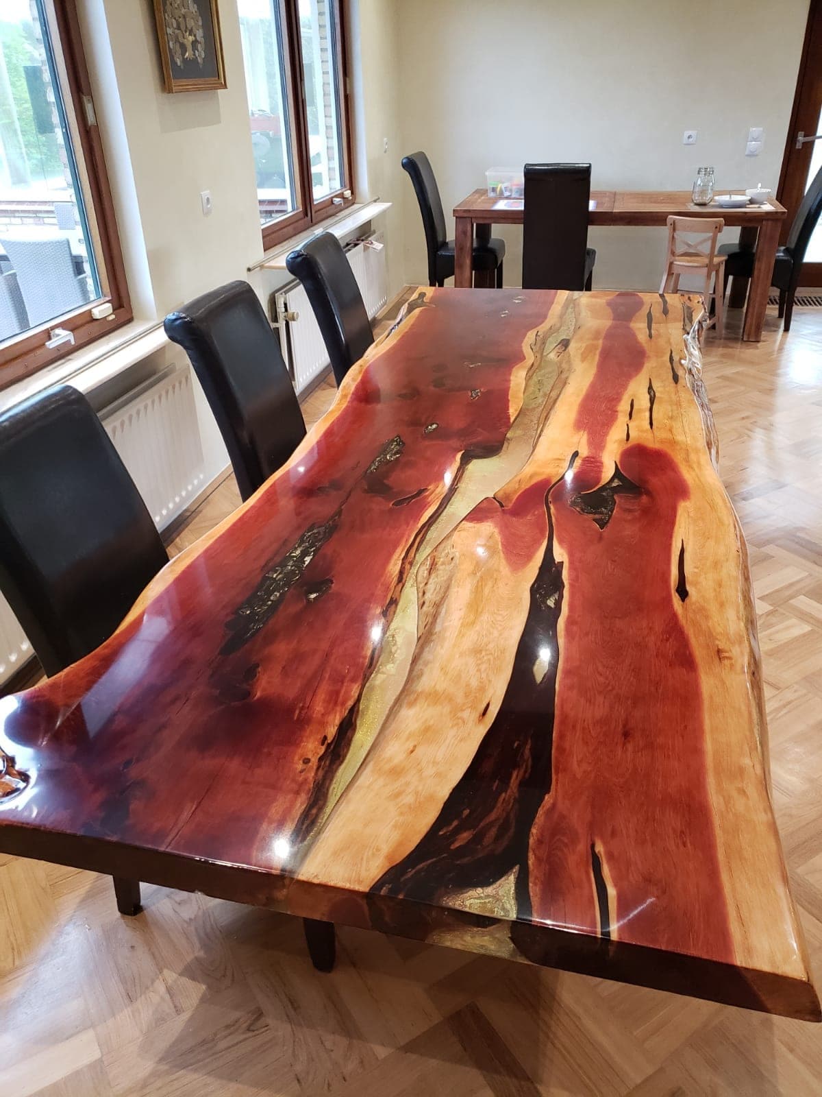 Vue plongeante en biais d’une table en genévrier aux bandes de bois rouges et jaunes, avec des cavités sombres et une résine brillante.