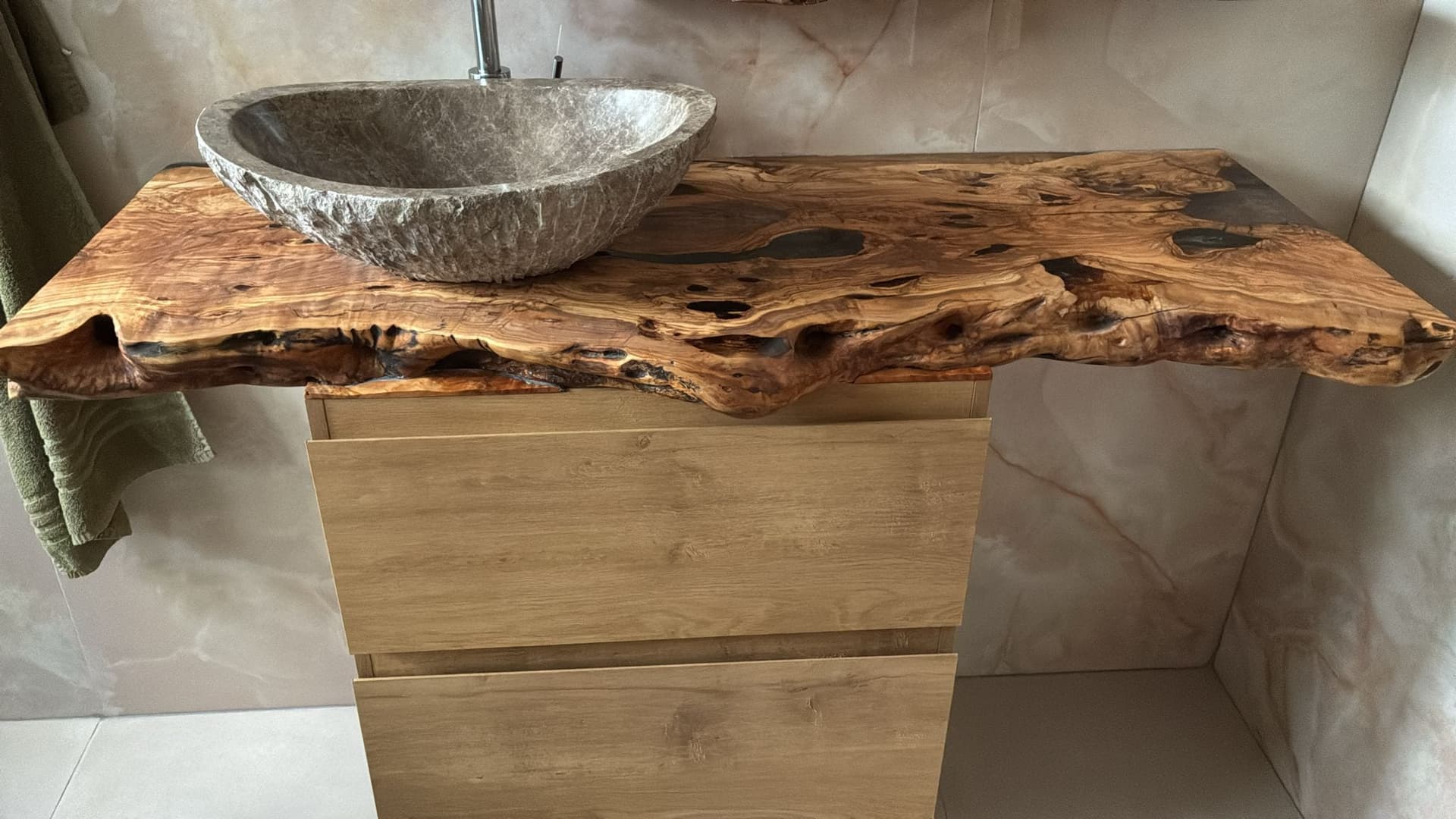 Olive wood vanity top with an irregular live edge, epoxy fills and a grey stone basin on the left above a wooden cabinet.